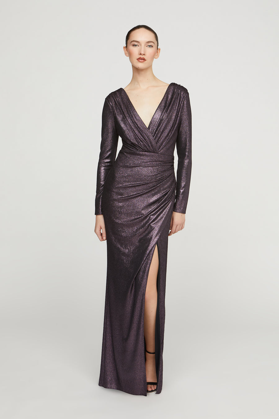Woman wearing a long, dark purple evening gown with a deep V-neck and slit on a white background