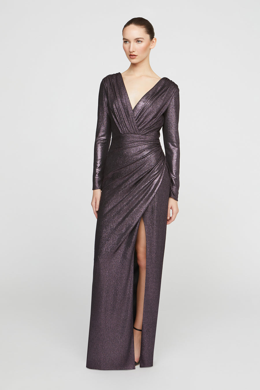 Woman wearing a long, dark purple evening gown with a slit on a white background